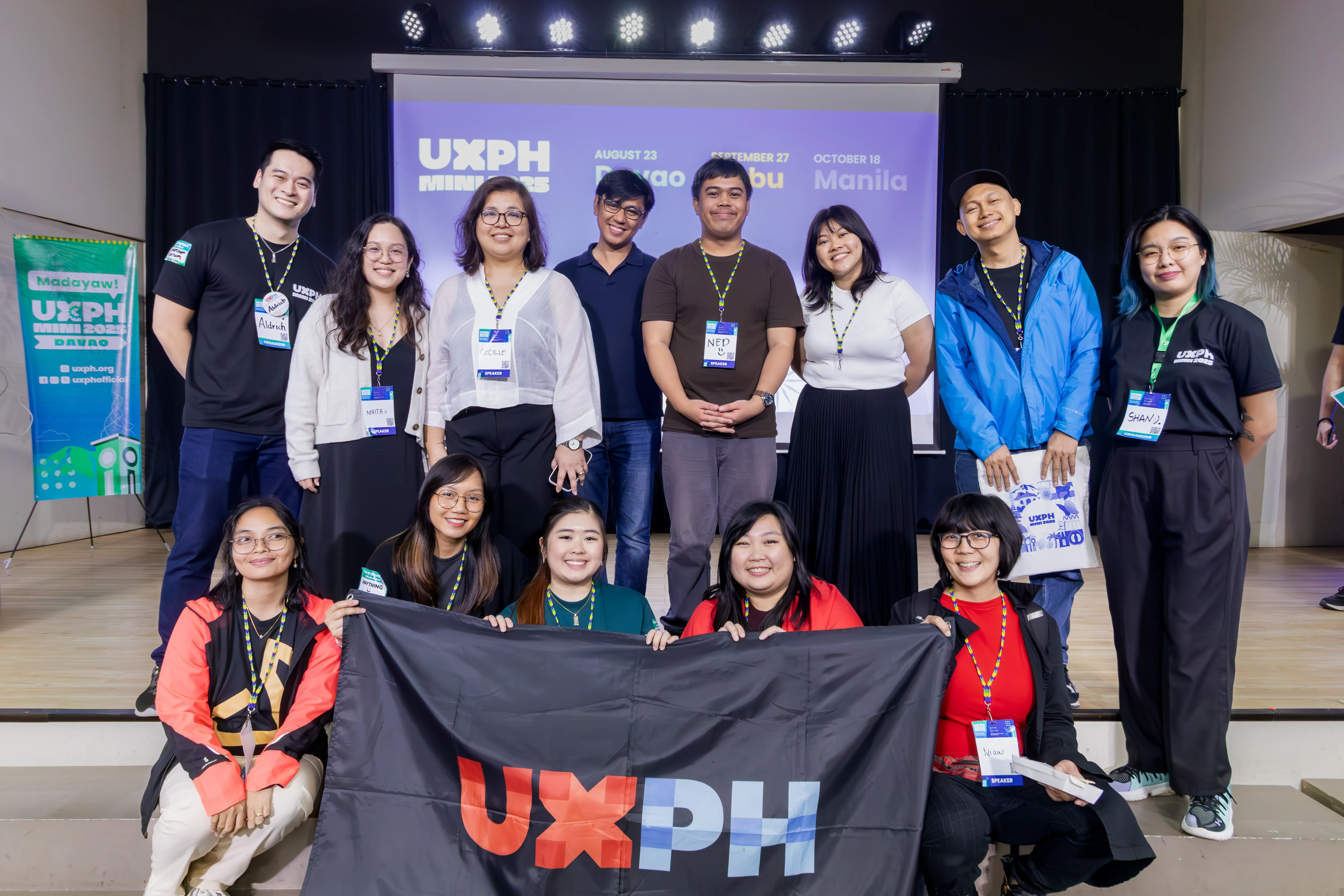 Group photo of the speakers, workshop facilitators, and the main organizers for UXPH Mini 2025: Davao. Chi is seated at the second row, helping hold up a black cloth flag with the UXPH logo printed on it.