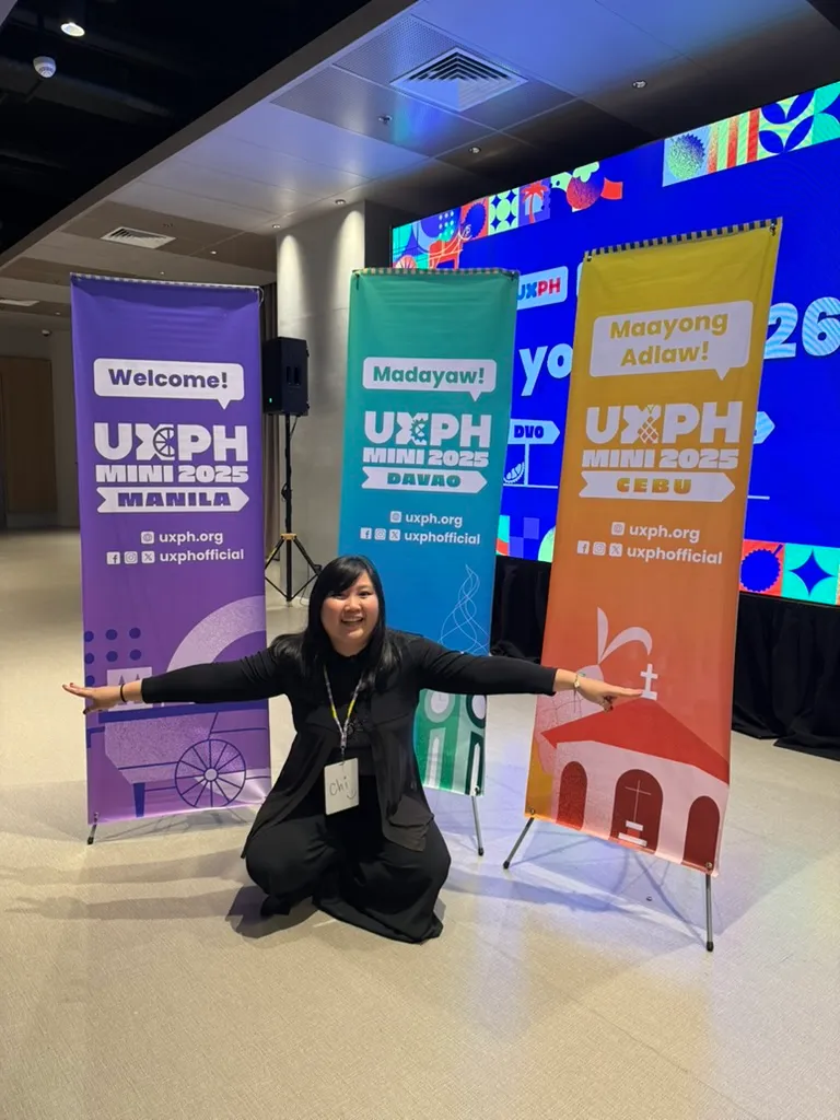 Chi posing in front of all 3 tarps for UXPH Mini 2025, with her arms stretched to the sides. The tarps behind her show, from left to right, the one for Manila, Davao, and Cebu legs.