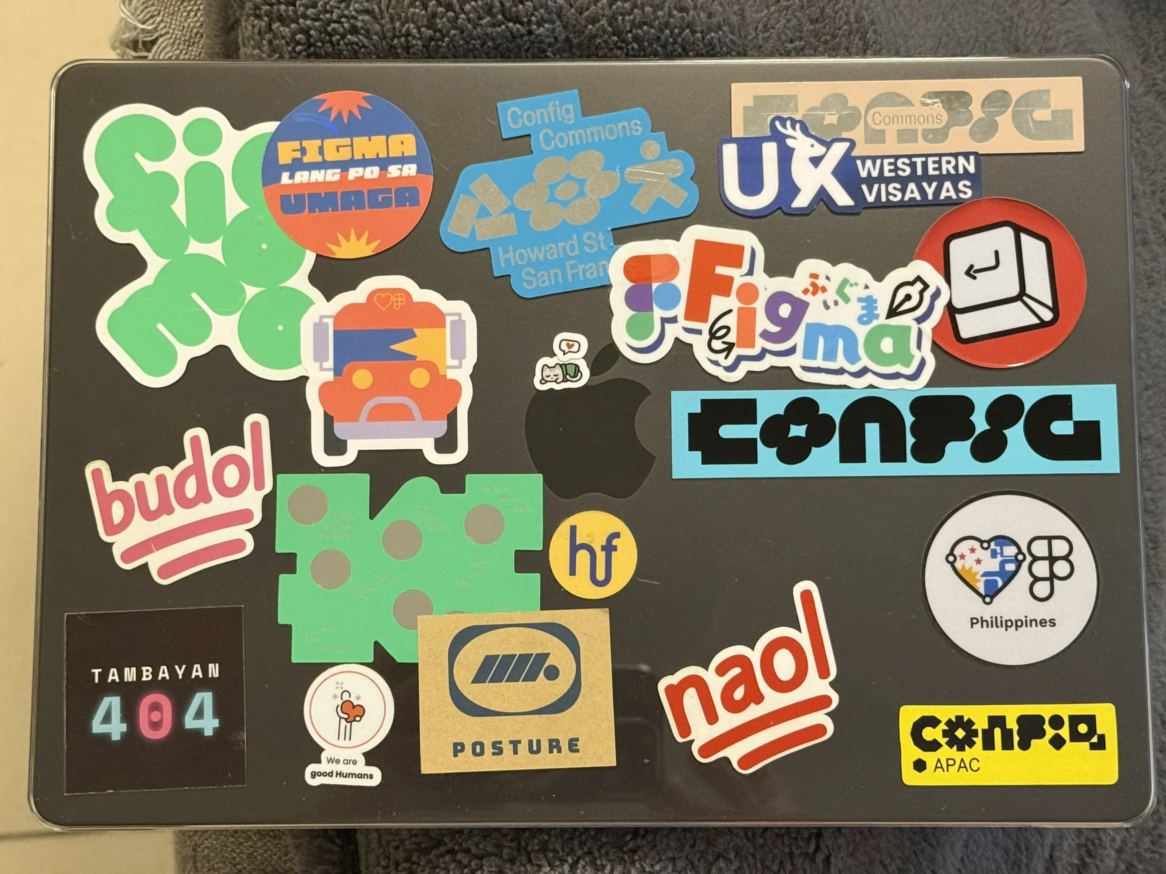 Top view of Chi’s MacBook cover decorated with colorful stickers featuring Figma logos, UX Western Visayas, Tambayan 404 (an online community she co-founded during the pandemic), Next Keyboard Club, Posture Works Atelier, and Humanforce. There are also playful “budol” and “naol” word emoji stickers among the mix.